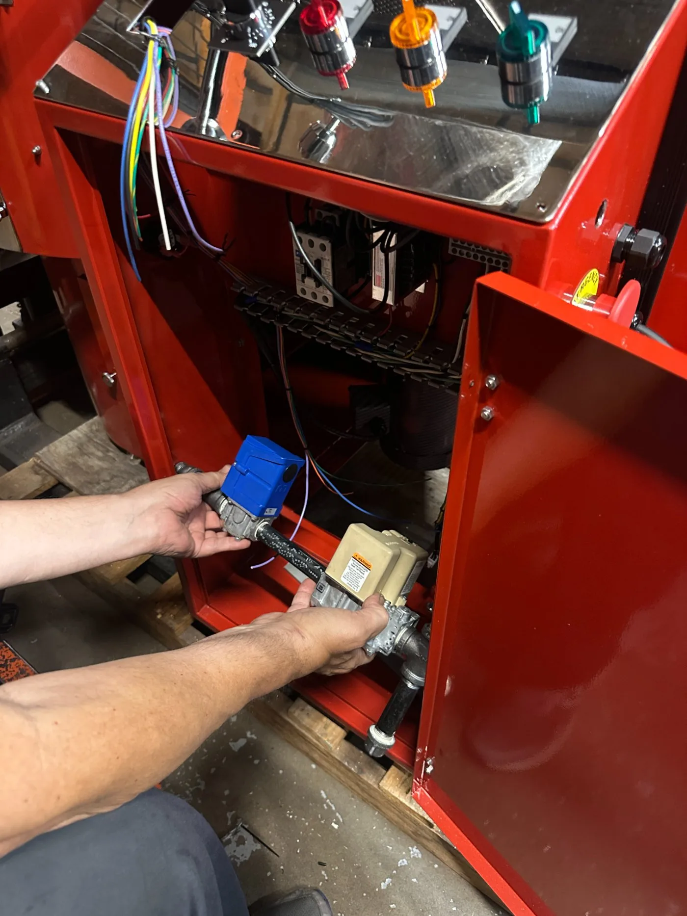 Hands fitting the gas train into an open roaster body in the Clearwater shop